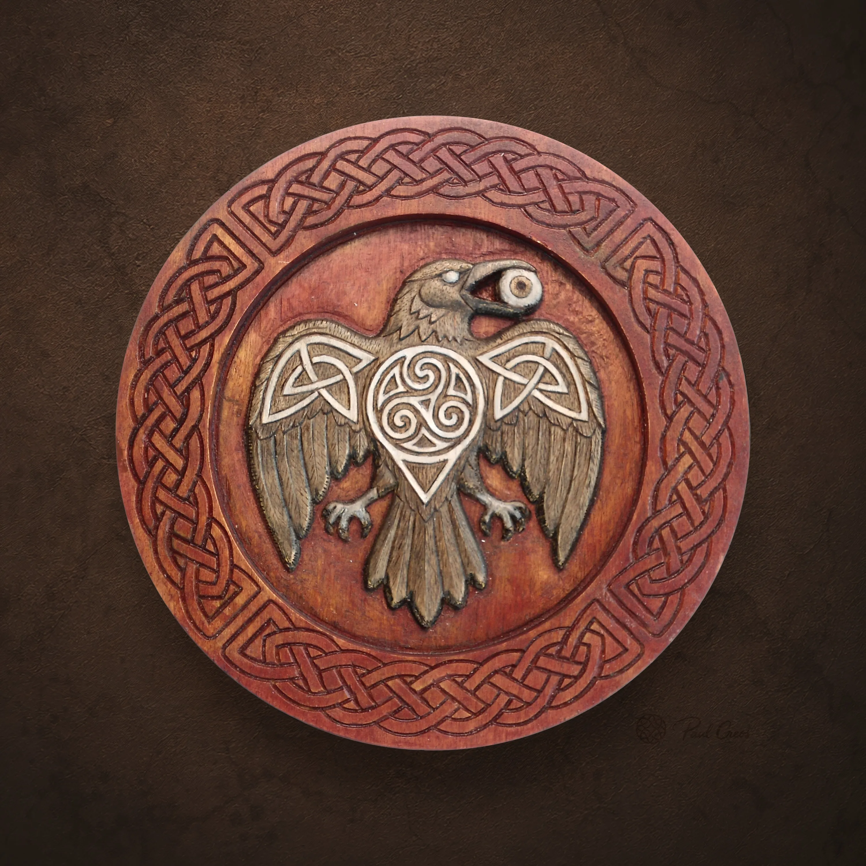 Raven Fire wooden roundel with a spread-winged raven, central triskele, and Celtic knotwork border
